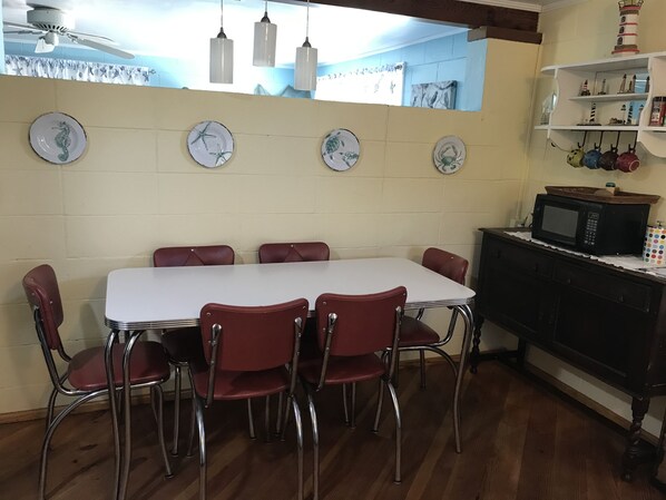 A dining area with a white table and red chairs, a ceiling fan, and decorative plates on the wall. - Secluded Florida Beach Bungalow-LAST MINUTE SPECIAL 20% OFF AUG/SEPT (Panacea)