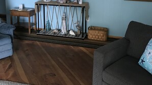 Een woonkamer met een blauwe wand, een houten salontafel, een grijze bank en een lijst met daarin een rivierafbeelding.