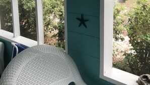 Een kamer met een witte geweven stoel, teal muren en een raam met een thermometer en decoraties van zeesterren.
