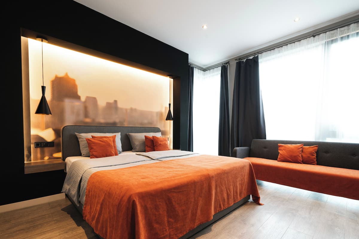 Une chambre moderne avec un grand lit, un canapé, une vue sur la ville et une représentation du paysage urbain sur le mur.