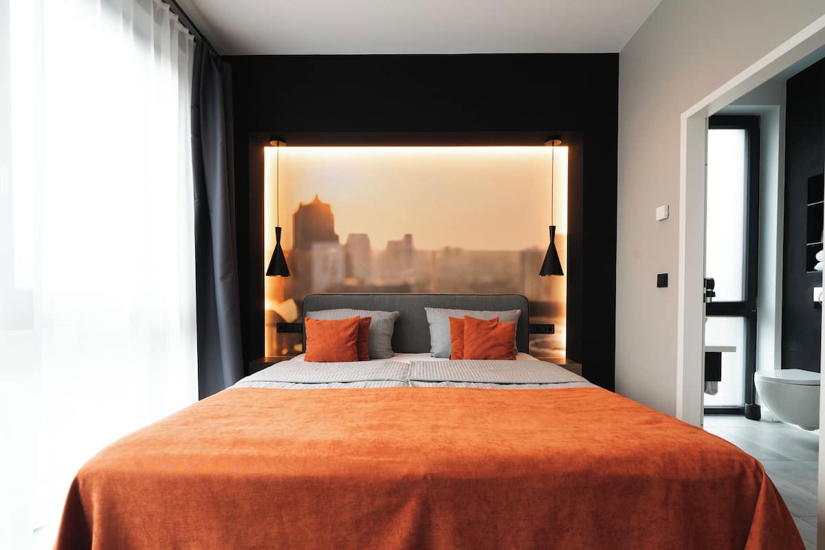 Une chambre d’hôtel moderne avec un grand lit, une vue sur la ville et deux lampes de chevet.
