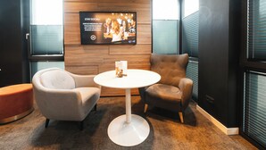 A modern lounge area with a round white table, two armchairs, and a wooden accent wall. - JustStay Grevenbroich Hotel & Apartments (Grevenbroich)