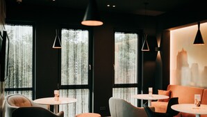 A modern interior with round tables and chairs, large windows with curtains, and pendant lighting. - JustStay Grevenbroich Hotel & Apartments (Grevenbroich)