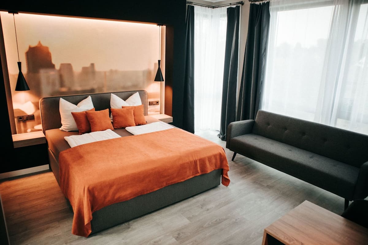 Une chambre d’hôtel moderne dotée d’un grand lit, d’un canapé, d’une vue sur la ville et d’une table de chevet avec une lampe.