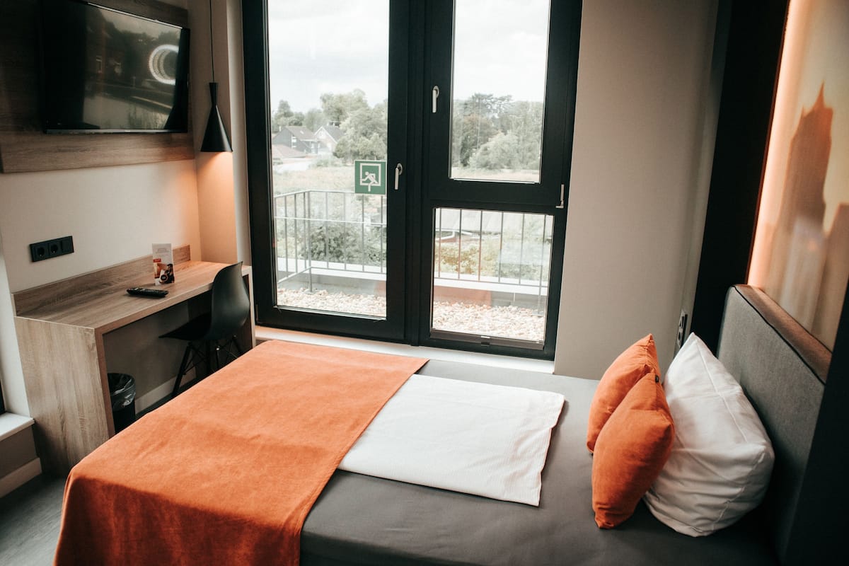 Une chambre d’hôtel équipée d’un lit, d’un bureau, d’un téléviseur fixé au mur et d’une fenêtre donnant sur l’extérieur.
