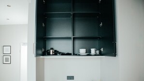 A kitchen with a black cabinet above a sink, a stove, and a countertop with a kettle and cups. - JustStay Grevenbroich Hotel & Apartments (Grevenbroich)