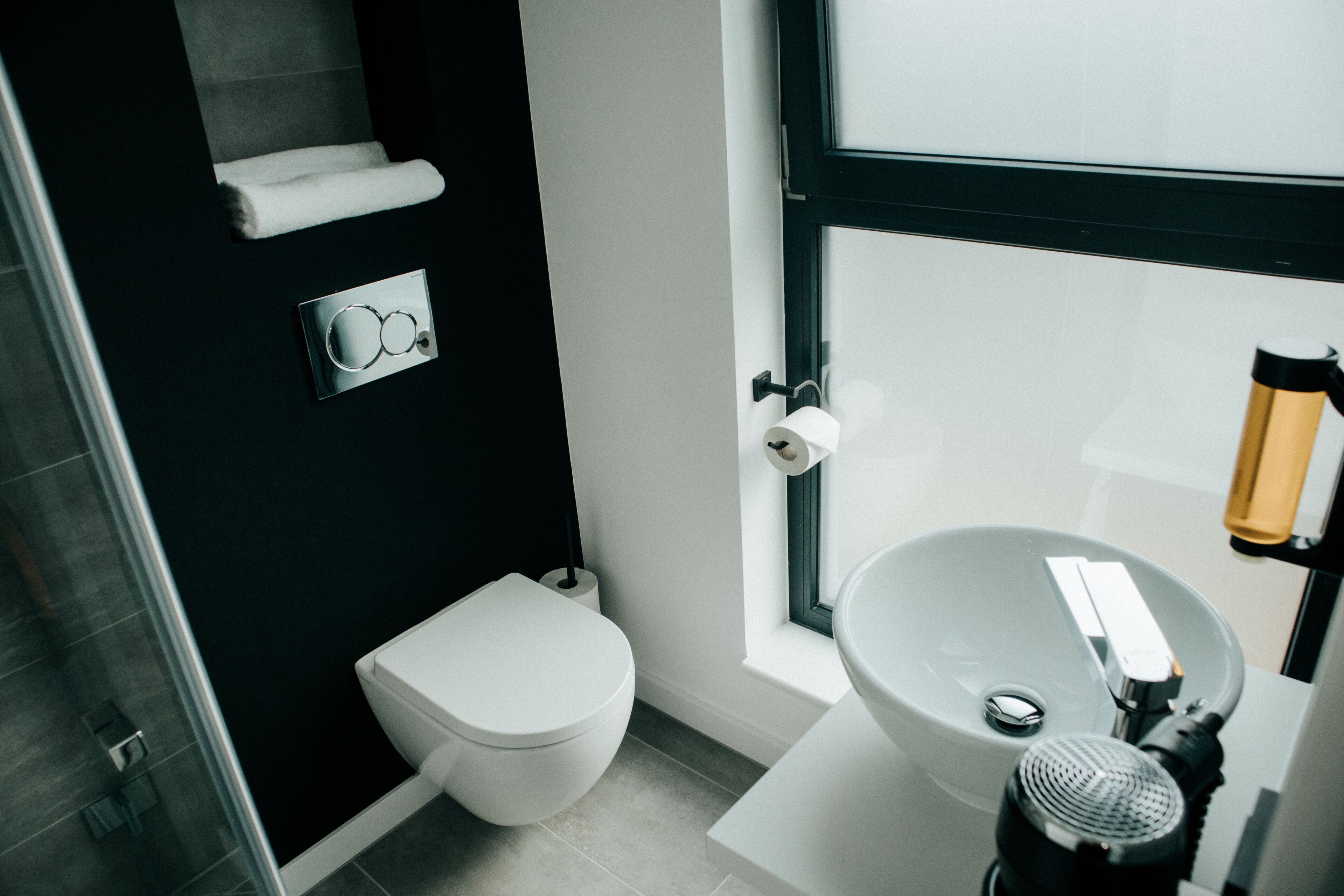 Un baño moderno con inodoro blanco, un lavamanos grande y un perchero para toallas.