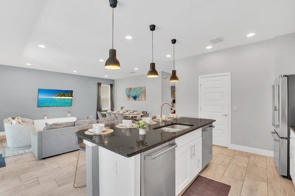A modern kitchen with a central island, stainless steel appliances, pendant lighting, and a dining area with a view.