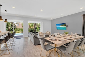Un comedor moderno con vista a la piscina, un televisor plano grande y una combinación de muebles para comer y relajarse.