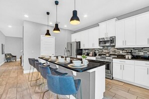 A modern kitchen with white cabinets, a central island with bar stools, and stainless steel appliances.