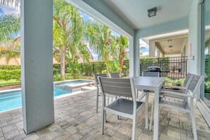 A covered patio area with a pool, outdoor seating, and a view of a residential neighborhood.