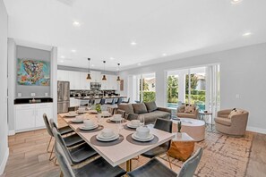 A modern kitchen with white cabinets, a dining area with a table set for six, and a living area with a sofa and armchairs.