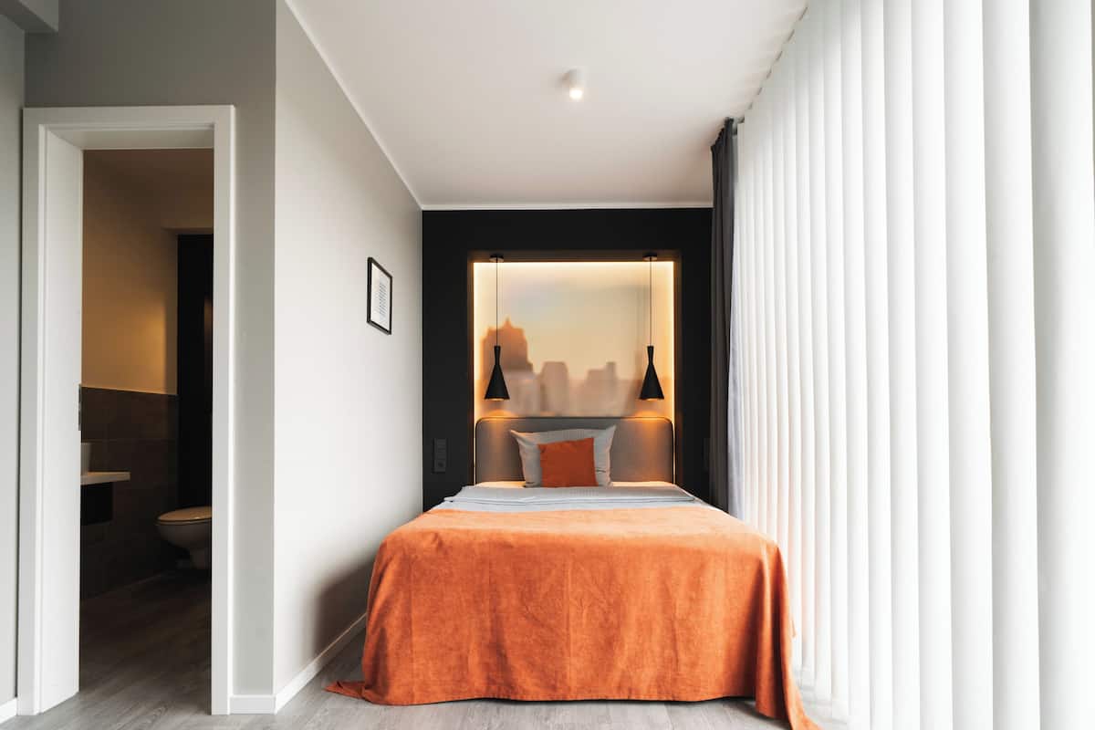 A modern hotel room with a large bed, a view of the cityscape through a window, and a separate bathroom area.