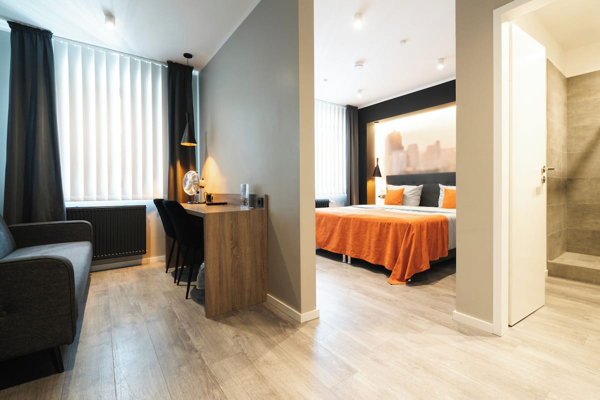 A modern hotel room with a wooden desk, a bed with orange bedding, and a cityscape view.