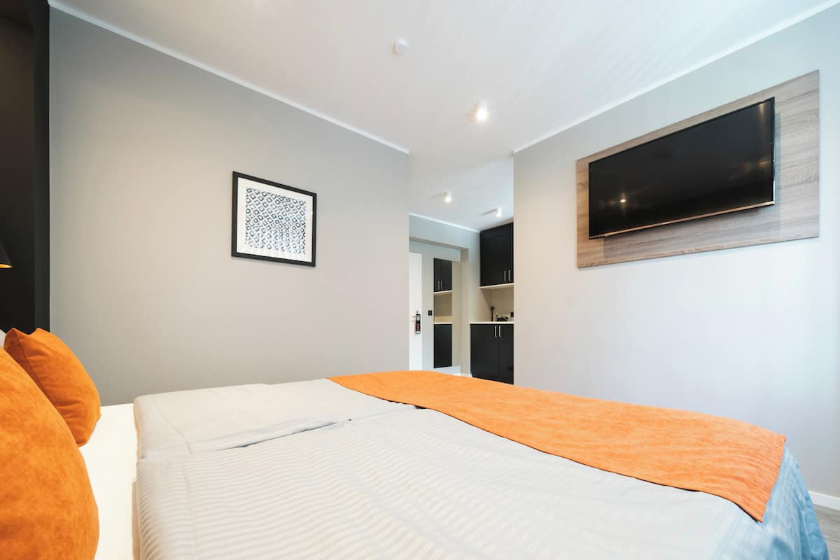 A modern bedroom with a large bed, a flat-screen TV mounted on the wall, and a framed artwork above the bed.