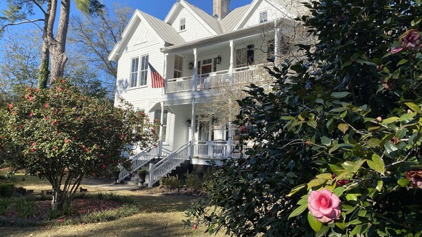 A two-story white house with a front porch, a staircase, and a flag.