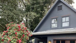 A two-story house with a dark blue exterior, a front door with a window, and a small brick structure in the front yard.
