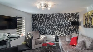 A modern living room with a glass coffee table, two grey sofas, a black TV, and a patterned wallpaper. - 2 Bedrooms Sleeps 6 Near Top Blackpool Attractions (Blackpool)