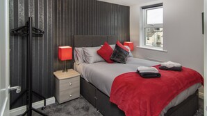 A modern bedroom with a bed, bedside lamps, a nightstand, a wardrobe, and a window with a city view. - 2 Bedrooms Sleeps 6 Near Top Blackpool Attractions (Blackpool)