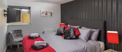 Un dormitorio moderno con una cama grande, una silla, una mesita de noche y un televisor montado en la pared.