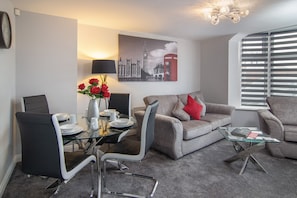 Un salon moderne avec une table basse en verre, un canapé gris et un coin repas comprenant une table et des chaises en verre.