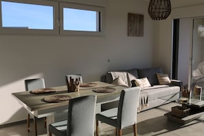 A modern dining area with a wooden table, grey upholstered chairs, and a grey sofa.