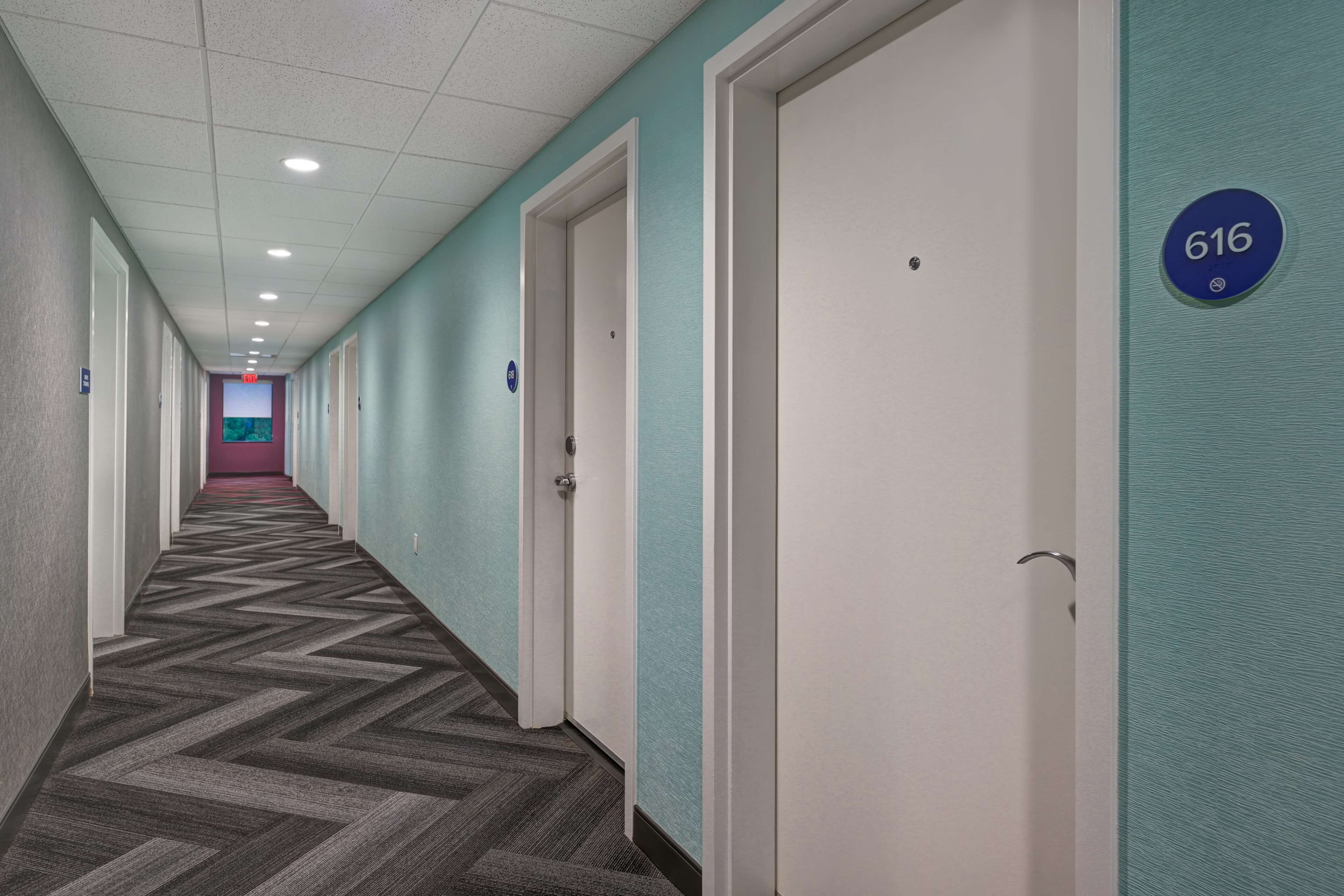 A hallway with doors marked by numbers, carpeted flooring, and a ceiling with recessed lighting.