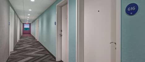 Un pasillo con puertas numeradas, piso alfombrado e iluminación empotrada en el techo.