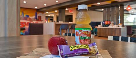 A meal with an apple, Tropicana apple juice, Nature Valley chewy, and an oatmeal raisin bar on a table in a hotel dining area.
