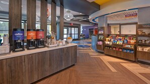 A modern hotel lobby with a coffee station, a snack bar, and a reception area.