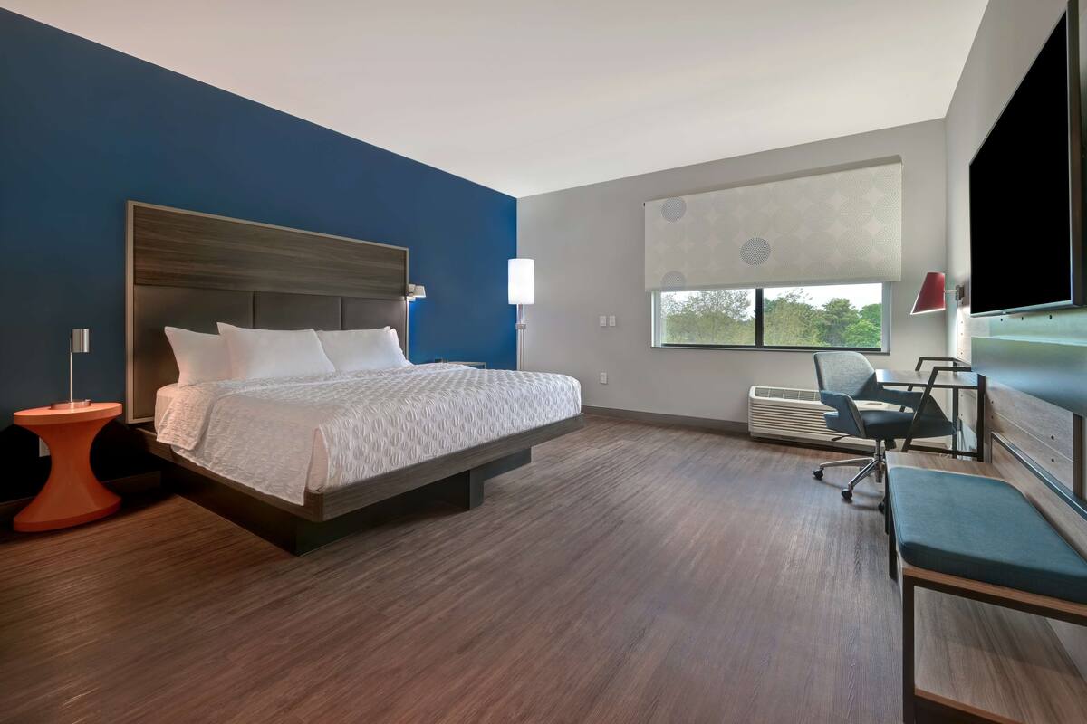 A modern hotel room with a large bed, a desk, and a chair.