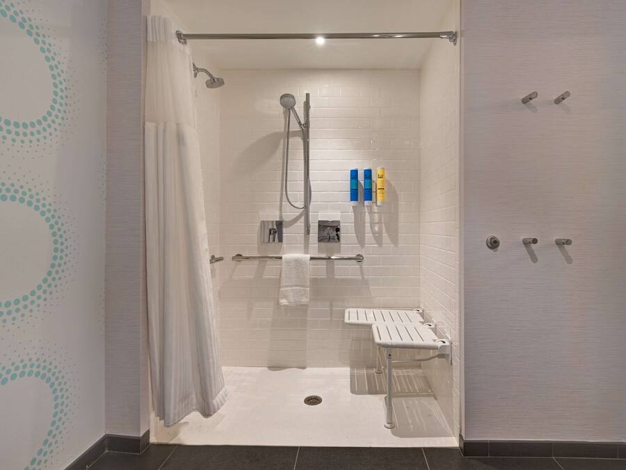 Ein modernes Badezimmer mit einer gläsernen Duschkabine, weißen Fliesenwänden, einem weißen Handtuchhalter und einer kleinen Ablage mit Toilettenartikeln.
