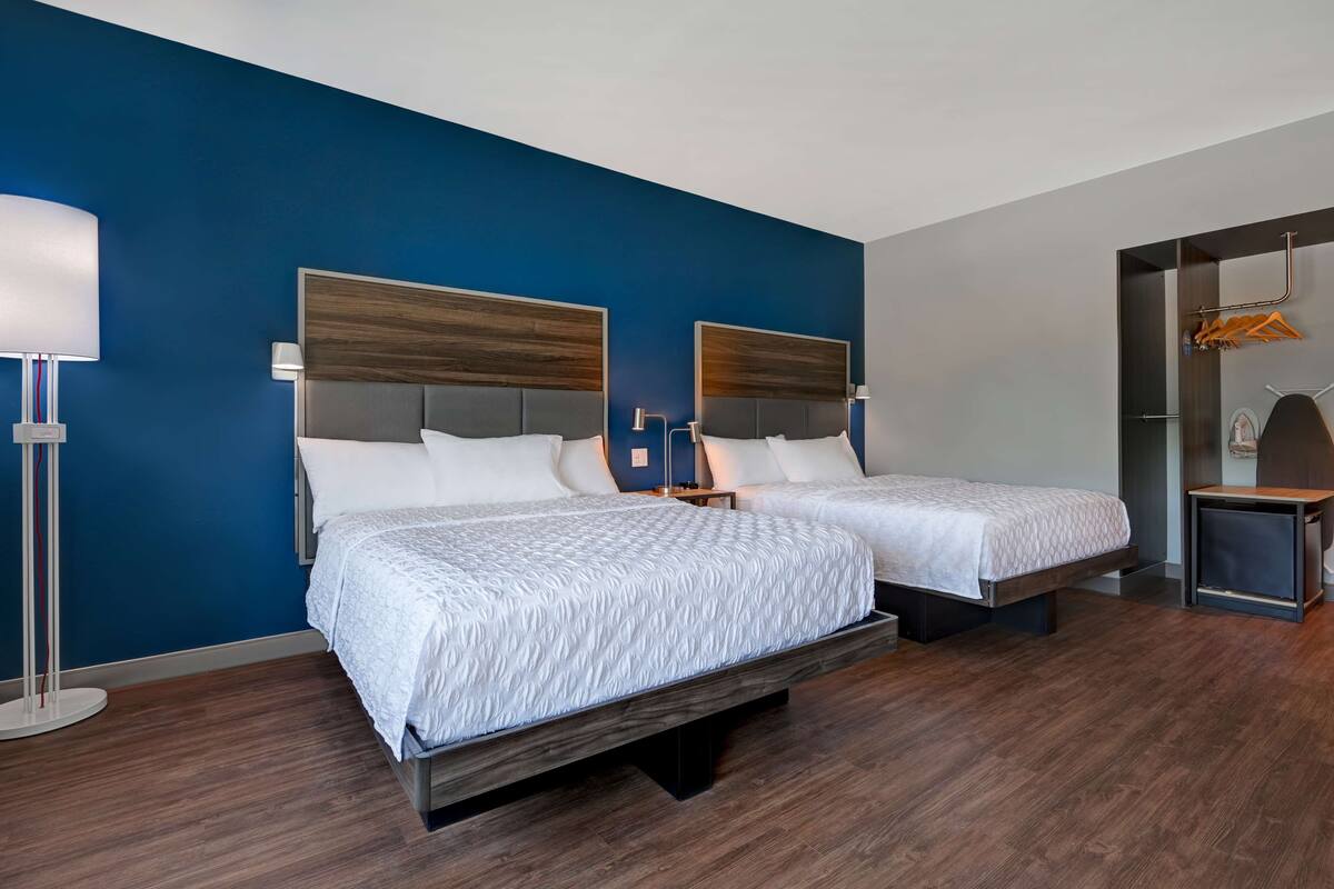 A hotel room with two beds, a large mirror, and a wardrobe with a hanging rack.