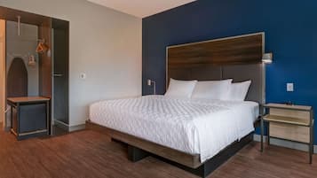 A modern hotel room with a large bed, a bedside table, a wardrobe, and a mirror.