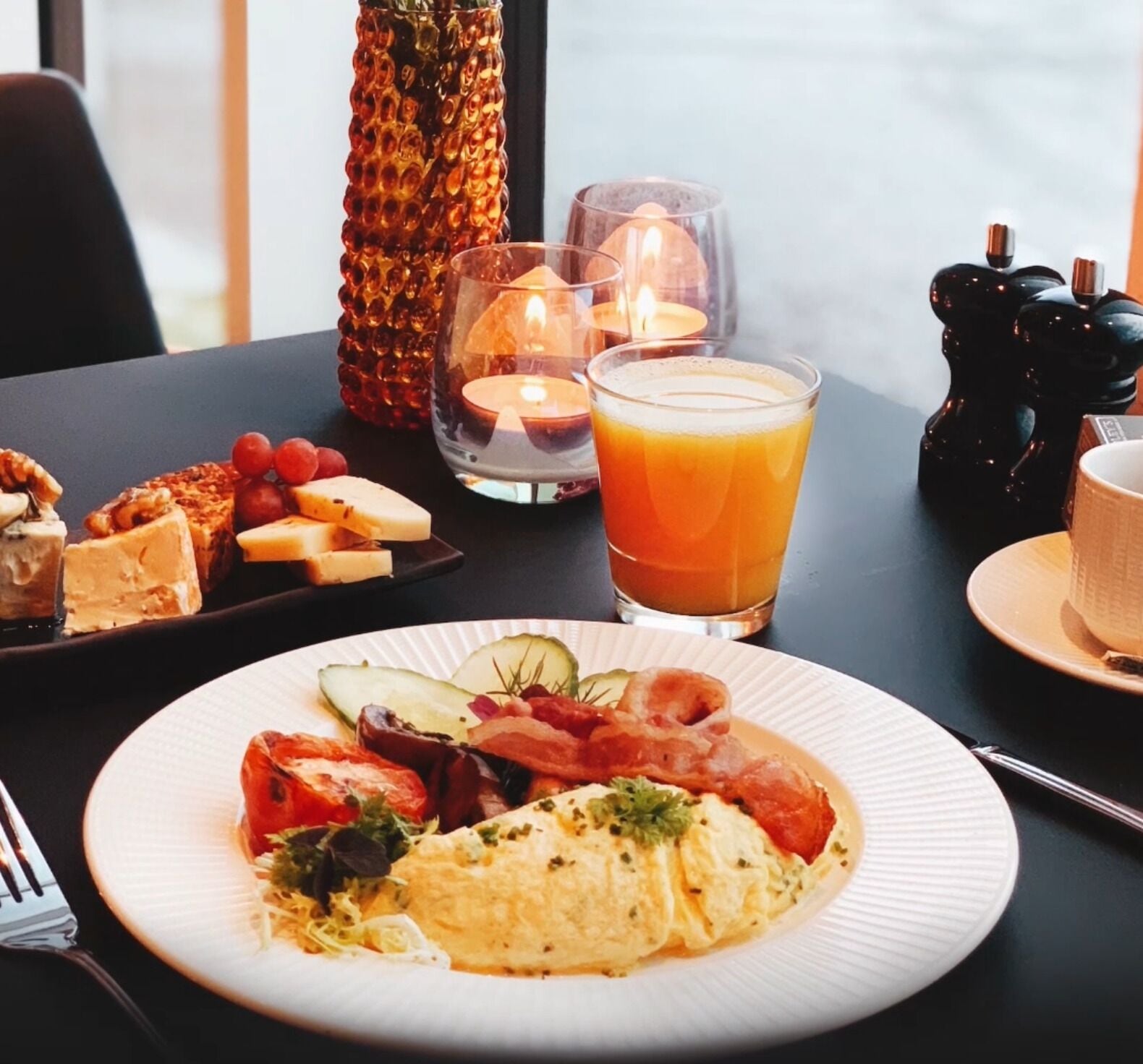 A breakfast setting with a plate of food, a glass of orange juice, and candles on a table.