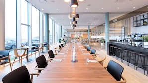 A modern dining area with a long wooden table, black chairs, and hanging pendant lights.