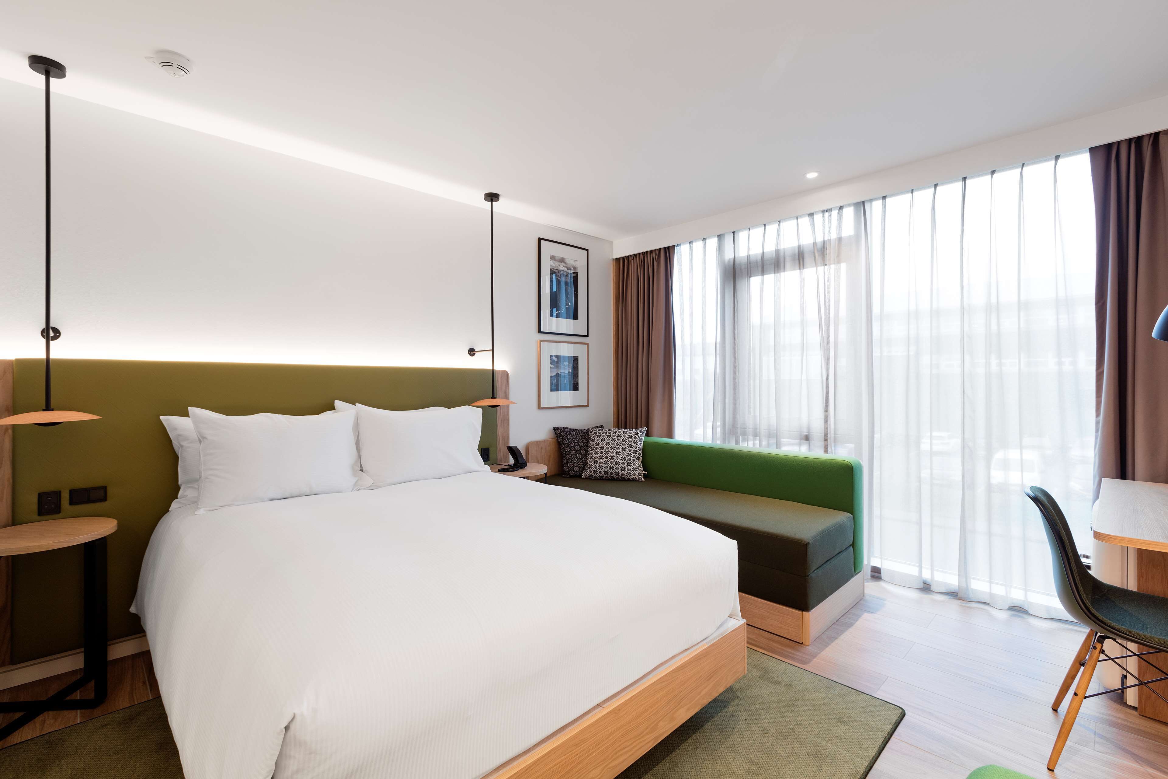 A modern hotel room with a large bed, a green sofa, a desk, and a chair.