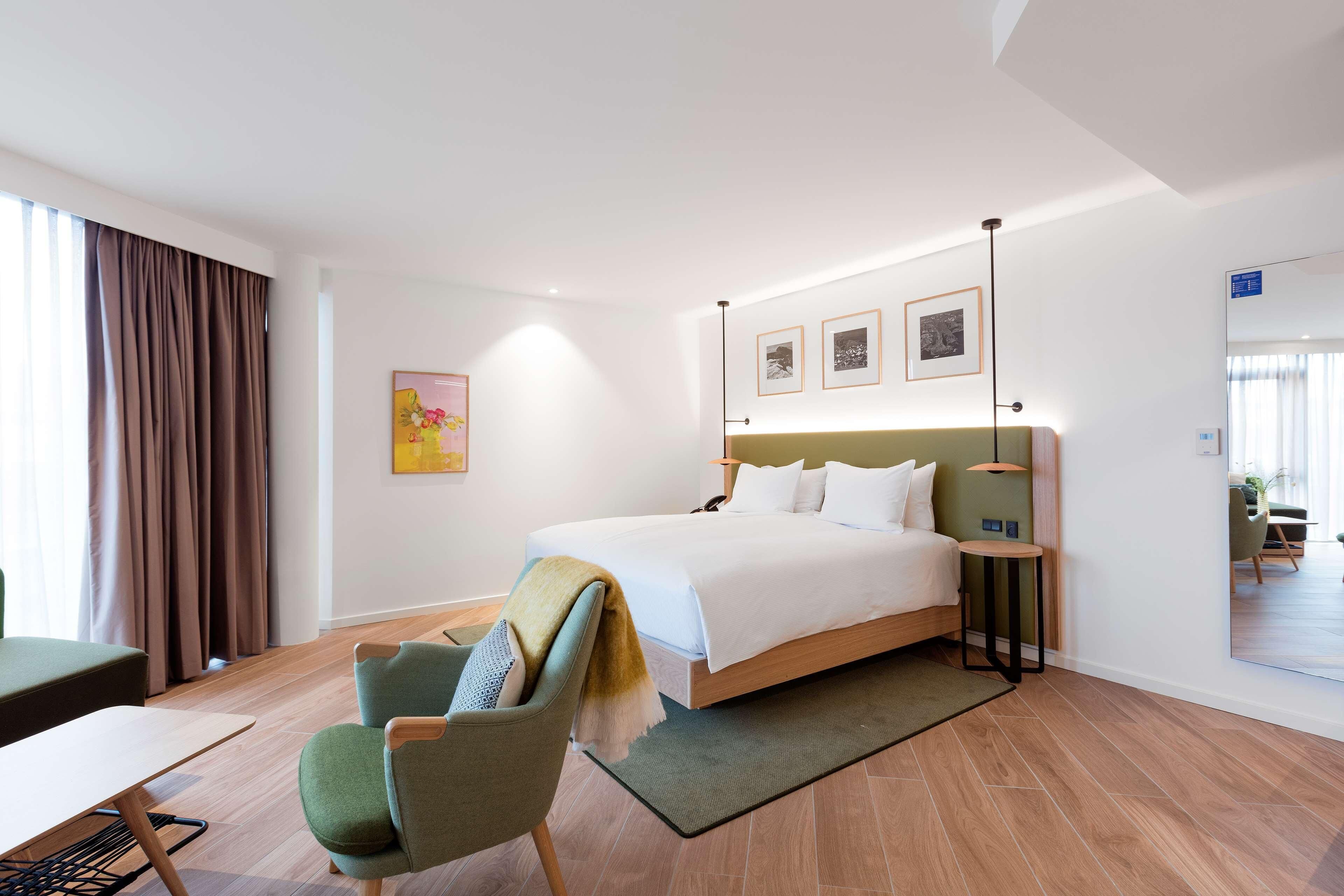 A modern hotel room with a large bed, a desk, a chair, and a small table.