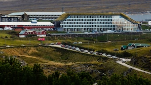 A modern building with a unique green roof and a parking lot with several cars.