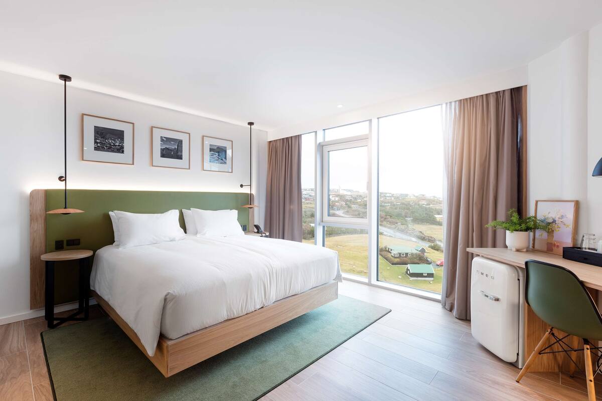 Una habitación de hotel moderna con cama, escritorio y ventanas amplias con vista a la ciudad.