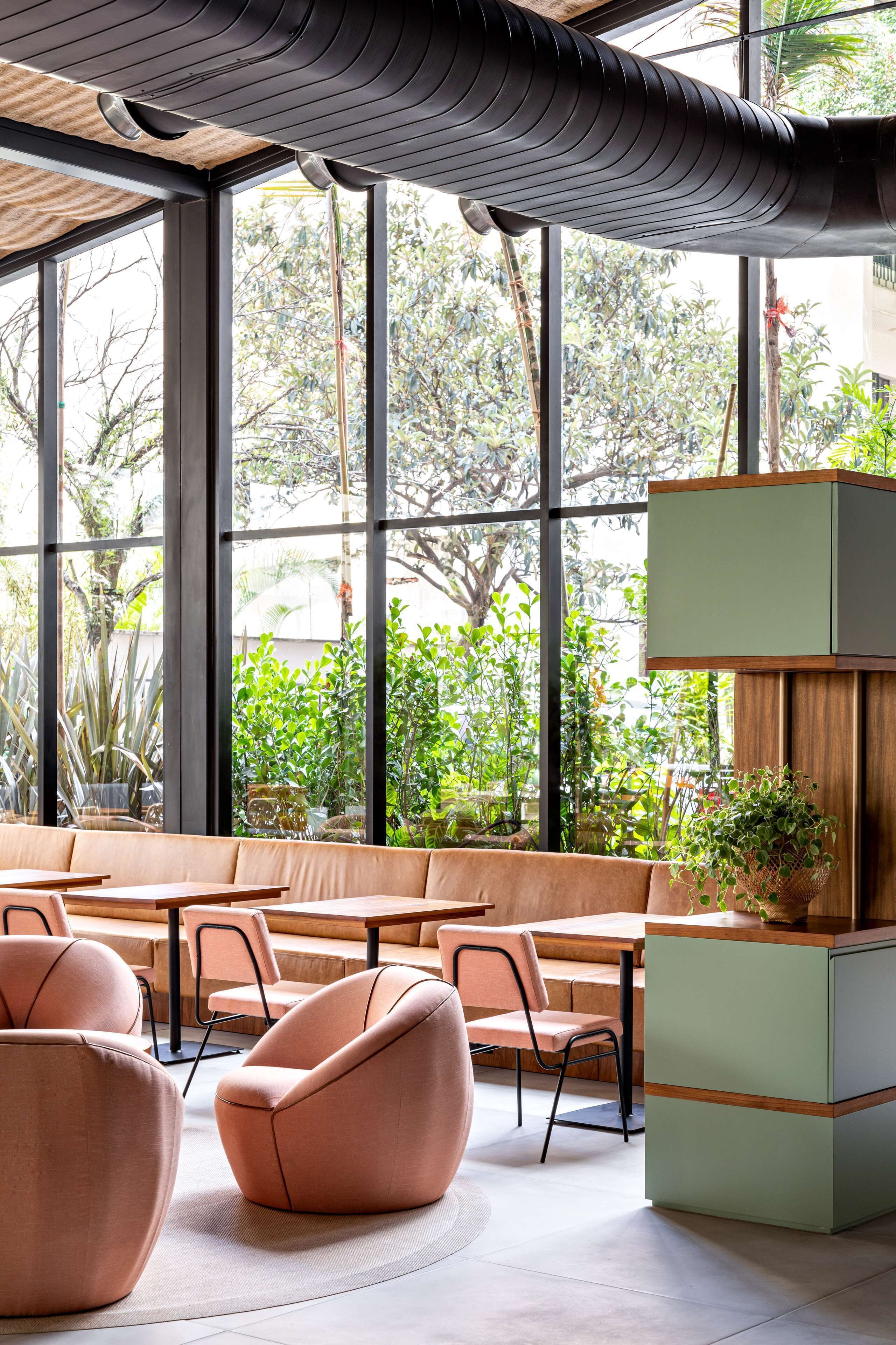 A modern indoor space with large windows, a wooden ceiling, and a seating area with cushioned chairs and tables.