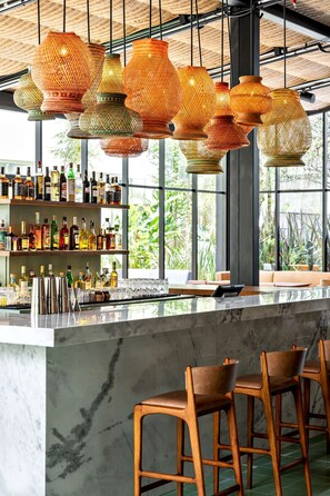 A bar area with hanging woven light fixtures, a marble countertop, and wooden bar stools. - Canopy by Hilton Sao Paulo Jardins (São Paulo)