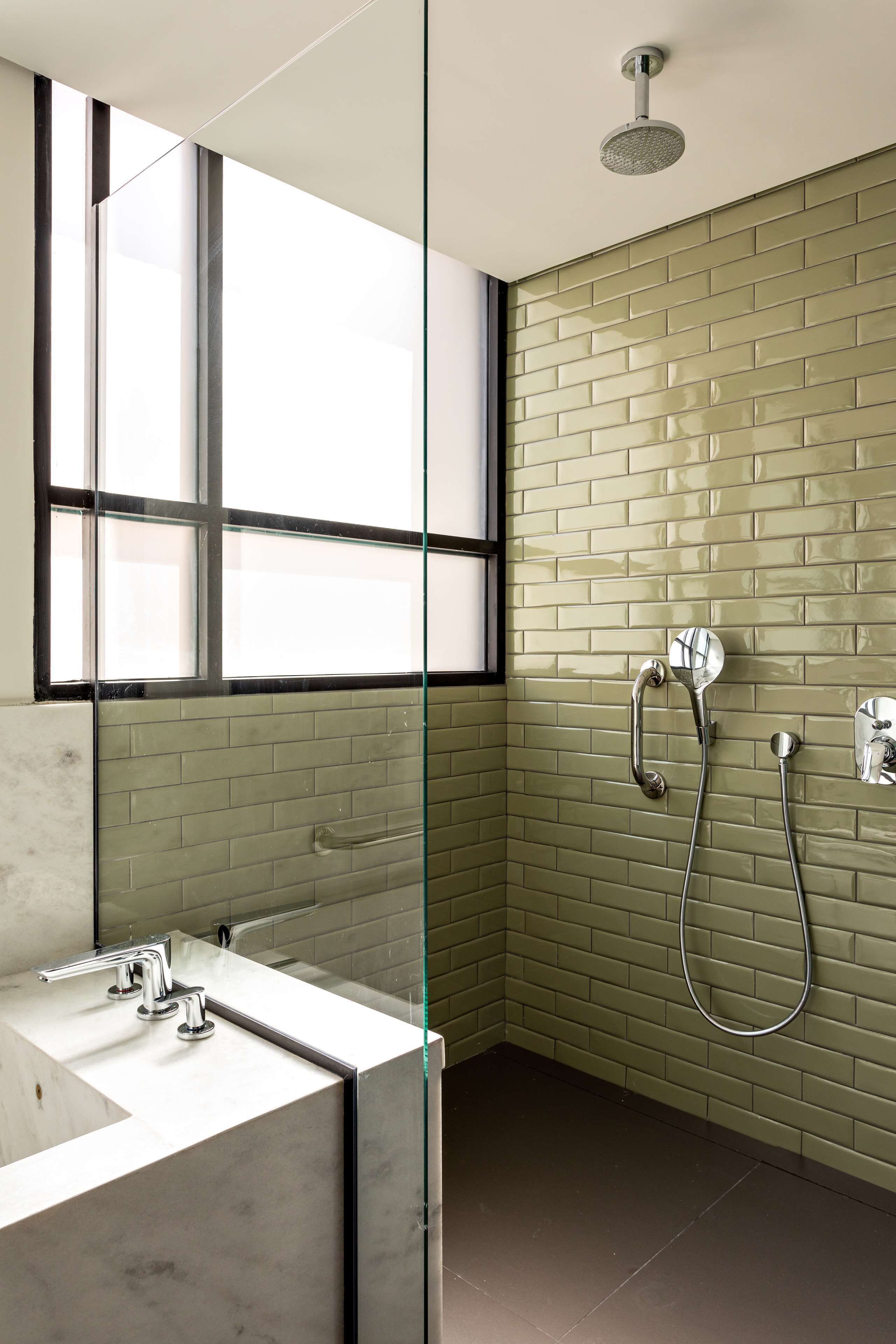 A modern bathroom with a glass partition, a large mirror, a shower with a handheld showerhead, and a tiled wall.