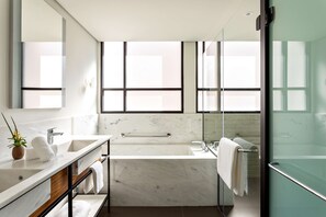 Un bany modern amb una banyera gran, un espai de banyera amb portes de vidre i un lavabo amb taulell de marbre.