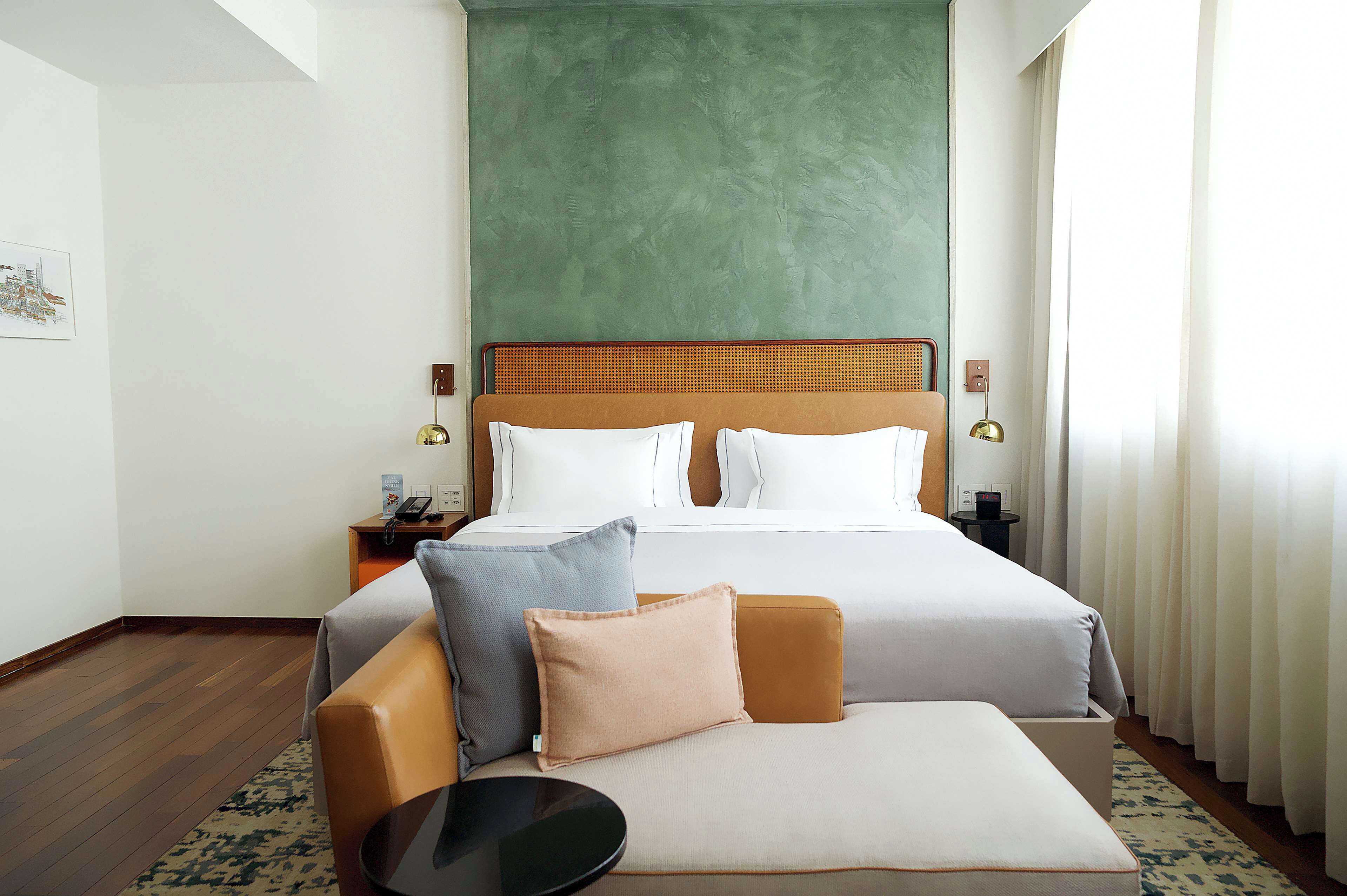 A hotel room with a bed, a nightstand, a lamp, and a sofa.