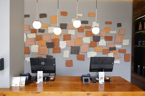 Taulell de recepció amb dos monitors HP, un comptador de fusta i una paret decorada amb dibuixos de paper de diferents colors i mides.