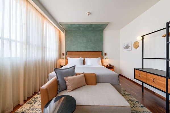 Habitació d'hotel amb un llit, un sofà, una taula de nit i una finestra gran amb cortines.