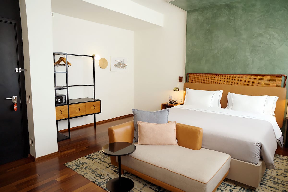 Habitación de hotel con cama, sofá, una mesita, armario y una pared de acento verde.