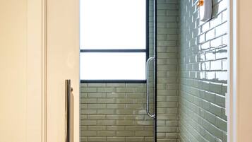 Bathroom features a glass shower enclosure, a towel on a stool, and a green-tiled wall.