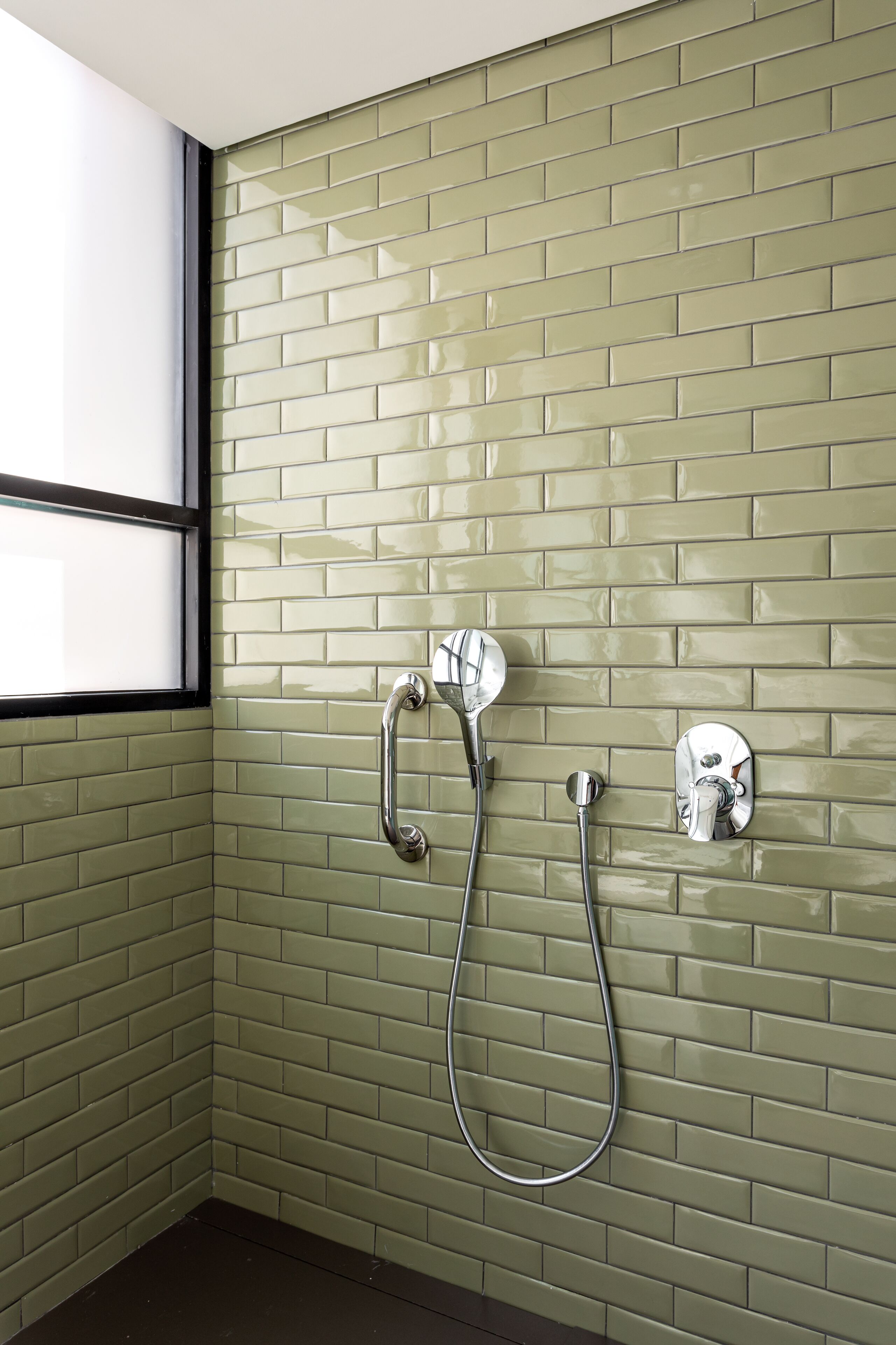 A bathroom with green tiled walls, a shower with a handheld showerhead, and a wall-mounted faucet.